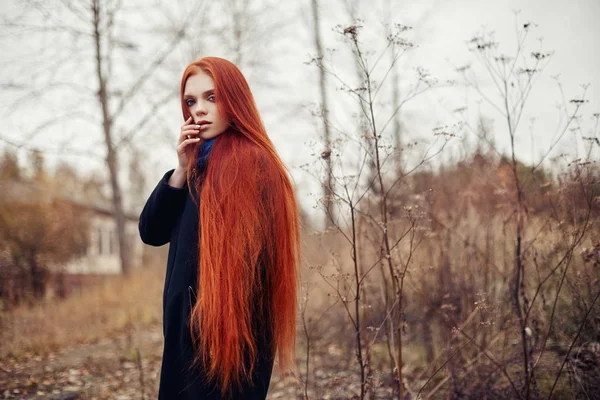 Mulher com longos cabelos vermelhos caminha no outono na rua. Olhar sonhador misterioso e a imagem da menina. Mulher ruiva andando no outono da cidade. Outono nublado frio na cidade . — Fotografia de Stock