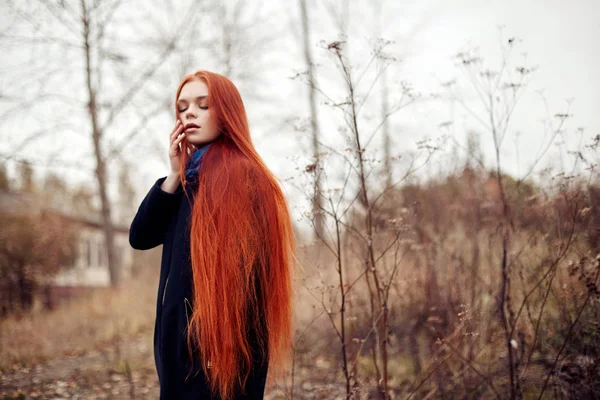 Donna con lunghi capelli rossi cammina in autunno per strada. Misterioso sguardo sognante e l'immagine della ragazza. Donna rossa a piedi in autunno la città. Autunno freddo e nuvoloso in città . — Foto Stock