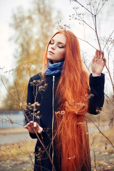 Donna con lunghi capelli rossi cammina in autunno per strada. Misterioso sguardo sognante e l'immagine della ragazza. Donna rossa a piedi in autunno la città. Autunno freddo e nuvoloso in città . — Foto Stock