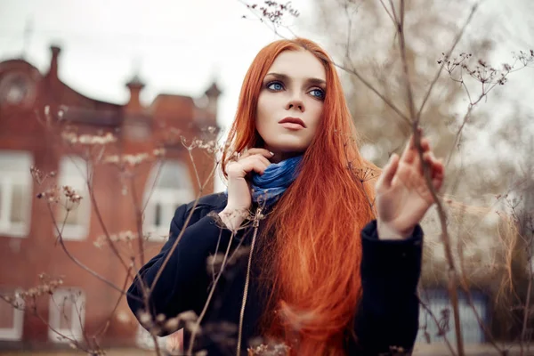 Frau mit langen roten Haaren geht im Herbst auf die Straße. geheimnisvoll verträumter Blick und das Bild des Mädchens. rothaarige Frau spaziert im Herbst durch die Stadt. kalter trüber Herbst in der Stadt. — Stockfoto