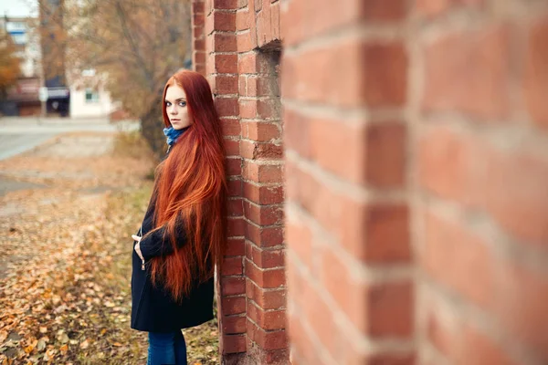 Mulher com longos cabelos vermelhos caminha no outono na rua. Olhar sonhador misterioso e a imagem da menina. Mulher ruiva andando no outono da cidade. Outono nublado frio na cidade . — Fotografia de Stock