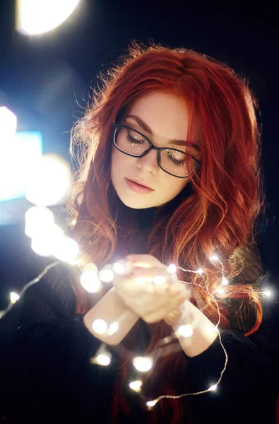 Kunstporträt einer Frau mit roten Haaren im Weihnachtslicht. Mädchen in Gläsern mit reflektierter Weihnachtsbeleuchtung. rote Haare in gelbem Licht, zarte Gefühle. Weihnachten kam. — Stockfoto