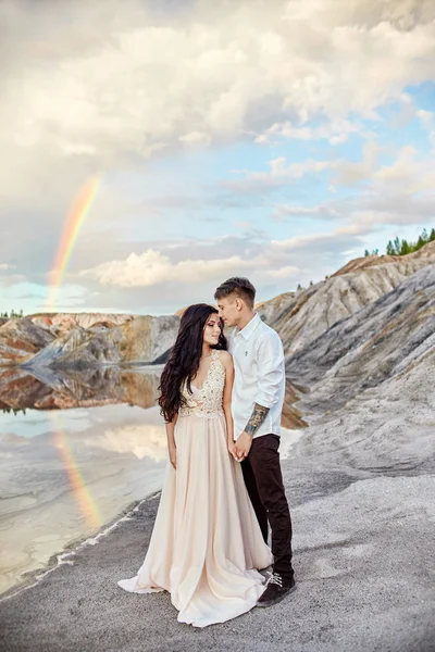 Casal apaixonado beijando e abraçando no fundo do arco-íris e montanhas. Um homem e uma mulher amam-se. Cenário fabuloso . — Fotografia de Stock