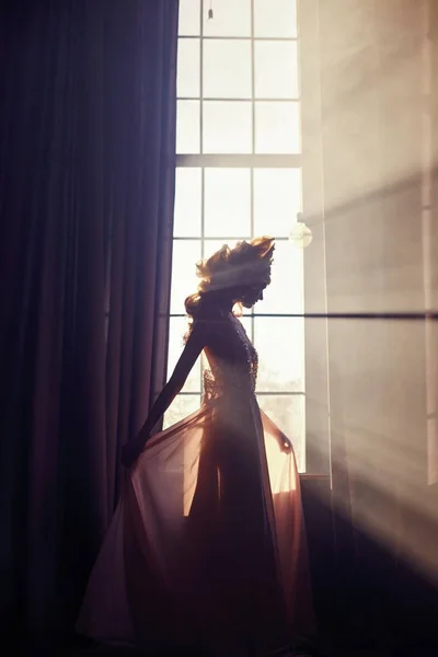 Vacker blond kvinna står i solljus vid fönstret i en lång b — Stockfoto