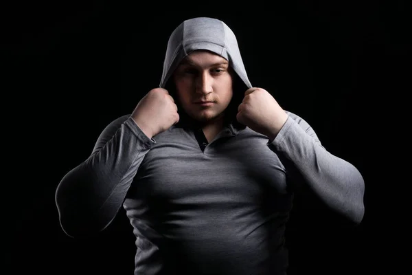 Большой мускулистый мужчина в капюшоне на черном фоне контрастность — стоковое фото