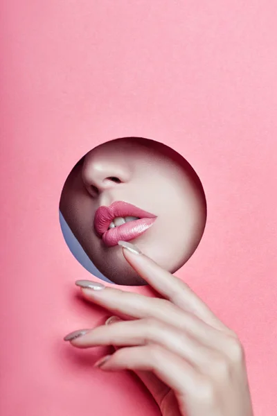 Bella ragazza con labbra paffute rosa sbircia attraverso un foro rotondo in carta rosa. Labbra e rossetto perfetti — Foto Stock