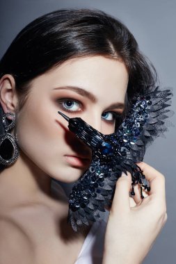 Siyah broş dekorasyon kuş şeklinde tutarak büyük mavi gözlü güzel esmer kız. Moda portre doğal makyaj mükemmel temiz cilt, yüz bakımı. Gençlik ve güzellik kadın, güçlü saç.