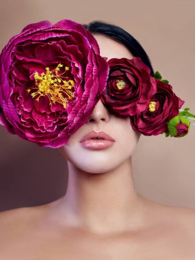 Bir kadın yakınındaki büyük peonies yüz, sanat moda çiçek bir kız, doğa yüz bakımı, doğal kozmetik ve profesyonel makyaj, bej renkli arka plan önünde. Saflık saç gözleri ve makyaj seksi kızlar.