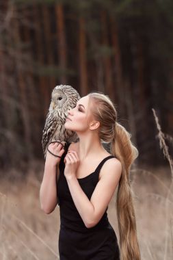 Sarışın kadın ile onun elinde bir baykuş sonbahar ve ilkbahar ormanda yürür. Uzun saçlı kız, romantik dikey, baykuş. Sanat moda fotoğrafı, güzel makyaj.