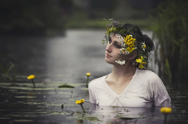 Konst kvinna med krans på huvudet i ett träsk i skogen. Våta häxa flicka i sjön, mystiska mystiska kvinna som badade utomhus i träsket. Krans av blommor på hennes huvud. — Stockfoto