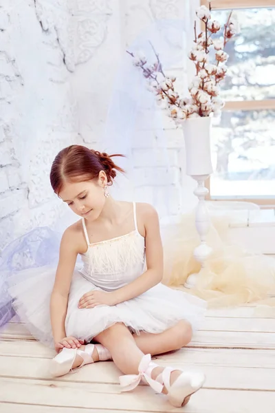 Un poco de ballet. La joven bailarina se está preparando para una actuación de ballet. Chica en un vestido de bola blanca y Pointe cerca de la ventana, hermoso pelo rojo. Joven actriz de teatro . —  Fotos de Stock