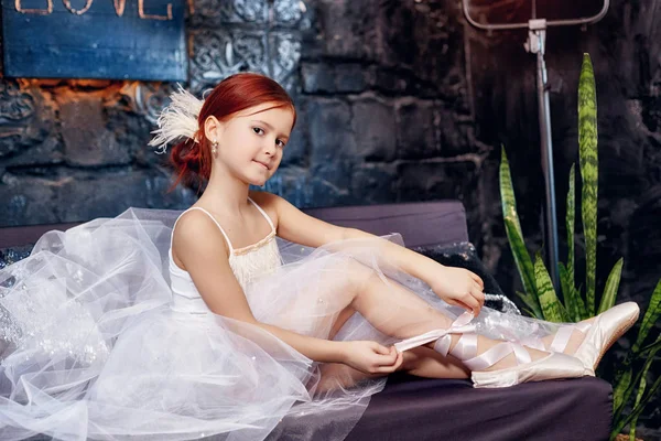 Girl in a white ball gown and shoes, beautiful red hair. Young theater actress. Little prima ballet. Young ballerina girl is preparing for a ballet performance. — Stock Photo, Image