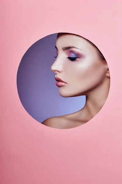 Beauty makeup cosmetics nature fashion woman in a round hole circle in pink paper, copy space advertising. Professional makeup perfect skin and shiny lipstick. Advertising banner, book cover. — Stock Photo, Image
