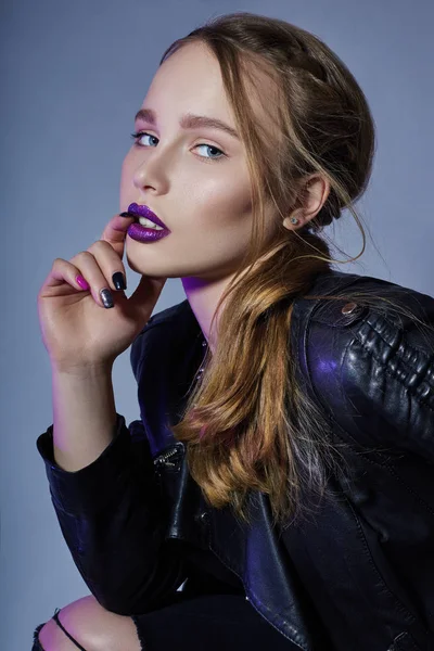 Mode Vogue fille maquillage rouge à lèvres violet, femme en veste en cuir et jean noir sur fond bleu foncé. audacieuse maquillage lumineux fille est mis en évidence avec la couleur pourpre . — Photo