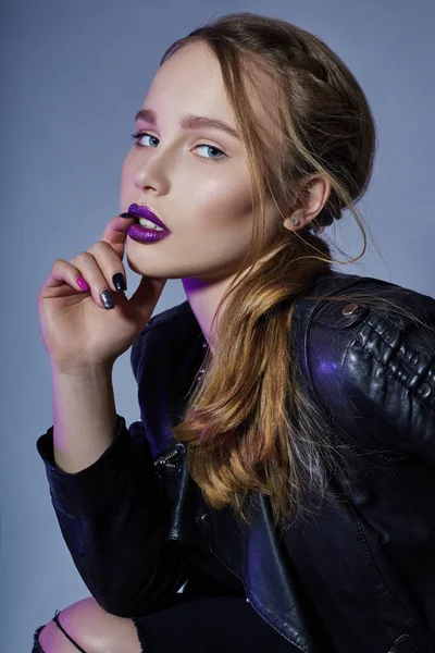 Moda Vogue menina maquiagem batom roxo, mulher de jaqueta de couro e jeans pretos no fundo azul escuro. Menina de maquiagem brilhante ousada é destacada com cor roxa . — Fotografia de Stock