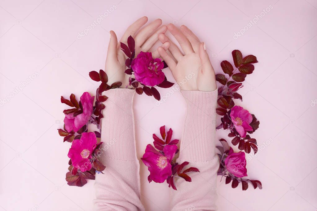Hand with pink flowers and petals lying on a paper background. C