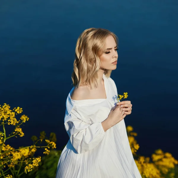 Ragazza in un lungo abito bianco con un fiore in mano si trova vicino — Foto Stock