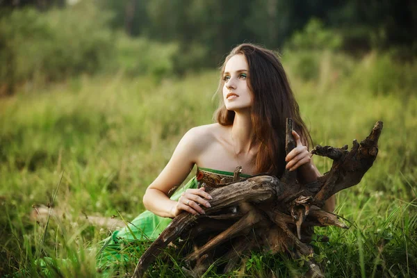 Dívka v krásných zelených šatech leží na trávě v blízkosti kořenů — Stock fotografie