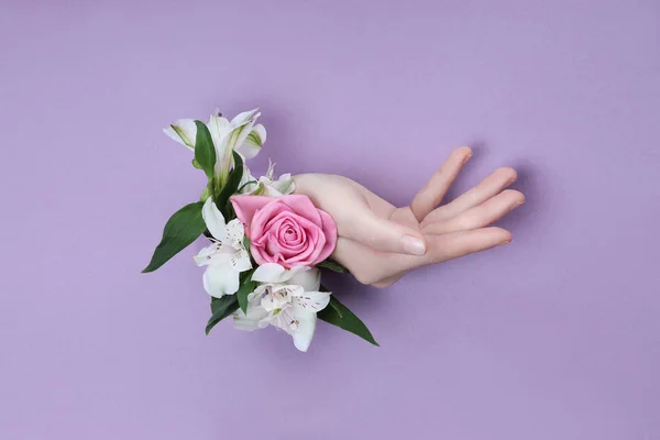 Schönheit Hand mit Blumen in einem Loch in einem lila Papierhintergrund. — Stockfoto