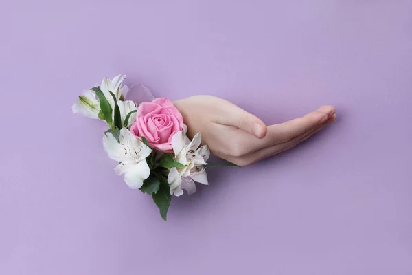 Belleza Mano con flores en un agujero en un fondo de papel morado . —  Fotos de Stock