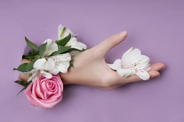 Belleza Mano con flores en un agujero en un fondo de papel morado . —  Fotos de Stock