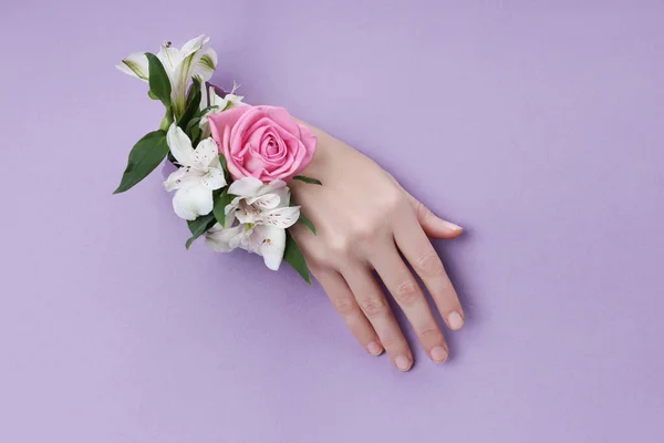 Beauty Hand met bloemen in een gat in een paarse papieren achtergrond. — Stockfoto