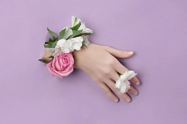 Beauty Hand z kwiatami w dziurze w fioletowym tle papieru. — Zdjęcie stockowe