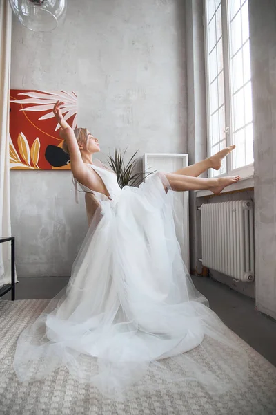 Bride woman in a light summer wedding dress sitting at the window and waiting for the wedding ceremony. Girl with perfect hair and beautiful makeup