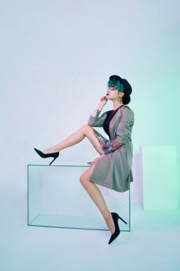 Şapkalı, yaratıcı yeşil saçlı, makyajlı, zehirli saçlı bir kadın. Kızın kafasında parlak renkli kıvırcık saçlar, profesyonel makyaj. Pelerinli dövmeli kadın.