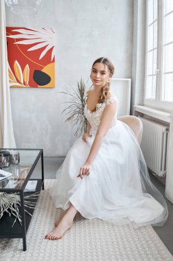 Açık yaz gelinlikli gelin, pencerede oturuyor ve düğün törenini bekliyor. Mükemmel saçlı ve güzel makyajlı bir kız.