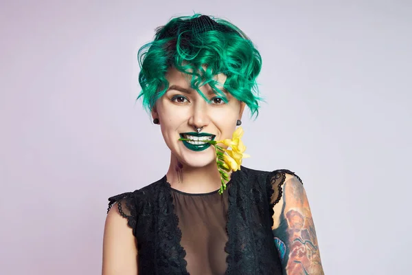 Woman with creative green coloring hair and makeup, toxic strands of hair. Bright color curly hair on the girl head, professional makeup. Woman with tattoo