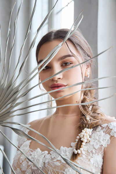 Bride is a woman in a light summer wedding dress standing at the window. Brown-haired girl with perfect hair and beautiful makeup