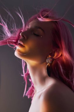Pembe saçlı, yaratıcı bir kadın portresi. Parlak renkli röfleler ve yüzünde gölgeler, mücevherleri olan bir kız. Rüzgarda boyanmış saçlar