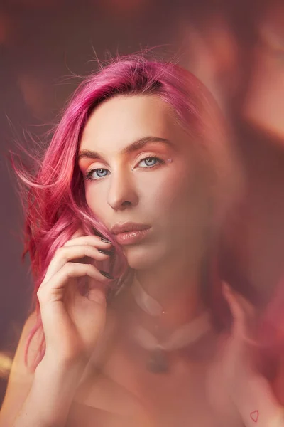 Art beauty portrait of a woman with pink hair, creative coloring. Bright colored highlights and shadows on the face, a girl with jewelry. Dyed hair in the wind