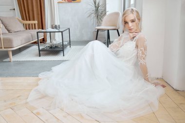 İdeal gelin yerde oturuyor, uzun beyaz elbiseli bir kızın portresi. Güzel saçlar ve temiz, yumuşak bir ten. Düğün saç stili sarışın.