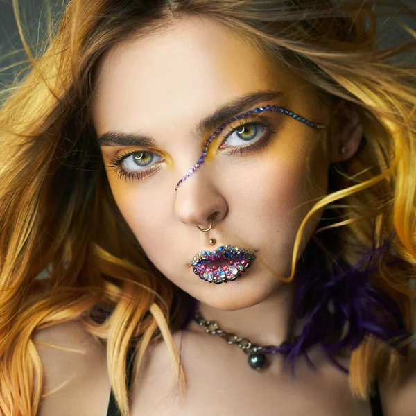 Woman with creative yellow coloring hair and makeup with rhinestones, purple strands of hair second layer. Bright color curly hair on the girl\'s head, professional makeup