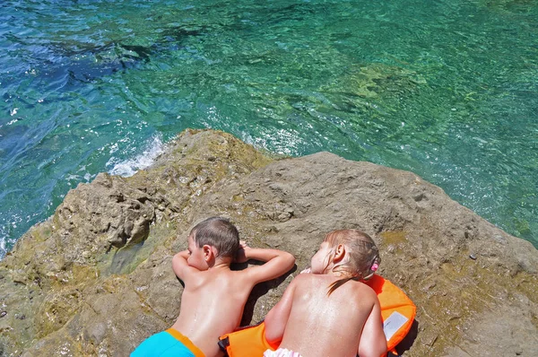 Un niño y una niña calentándose en la piedra después de nadar — Foto de Stock