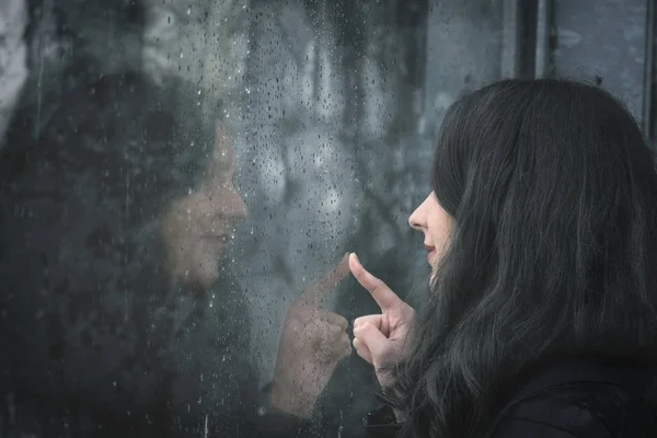 Vrouw en haar reflectie op regenachtige venster — Stockfoto