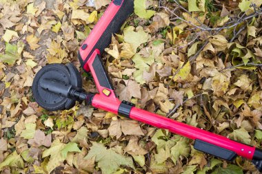 Escooter yerde kurumuş yapraklarla bırakılmış. Kırmızı escoote