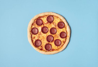 Mavi arka planda pizza salamı. Tam pizza pepperonisi. Yiyecek.
