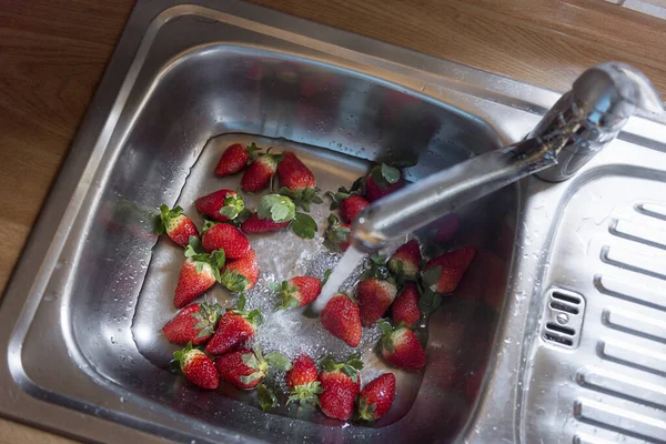 Strawberries pile in the kitchen sink. Washing fruits. Ripe berr