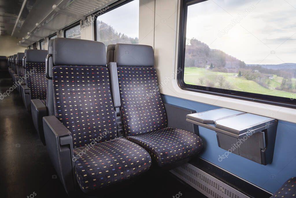 Swiss train interior with comfortable chairs, on two rows, a table and nature view on window. Public transport context. Passenger train interior.