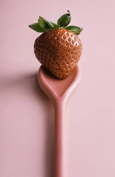 Ripe strawberry on a pink spoon, on a seamless background. One red berry close-up. Single organic strawberry. Sweet summer fruit.