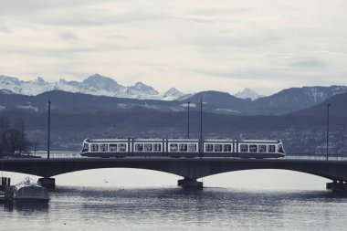 Zürih 'te bir köprüde toplu taşıma. Mavi saatte ufuktaki dağ sırası.
