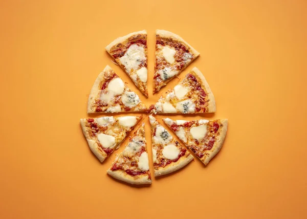 Cheese pizza cut in equal pieces on an orange seamless background. Flat lay of four cheese pizza. Quattro formaggi Italian pizza.