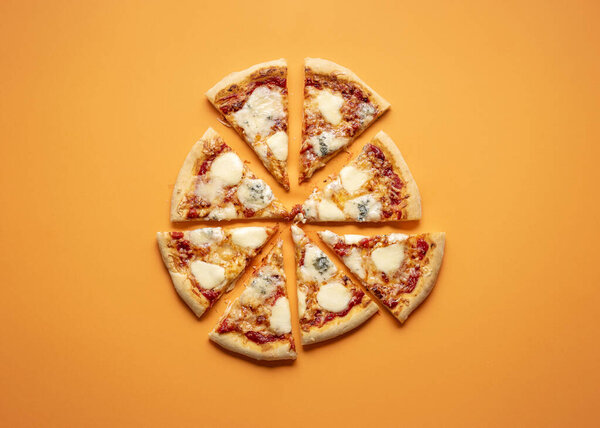 Cheese pizza cut in equal pieces on an orange seamless background. Flat lay of four cheese pizza. Quattro formaggi Italian pizza.
