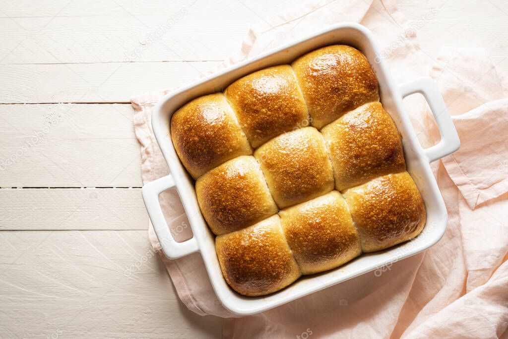 Pull apart bread buns in a white ceramic tray on a wooden table above view. Home-baked bread buns made with sourdough and white flour. Golden crust bread freshly baked.
