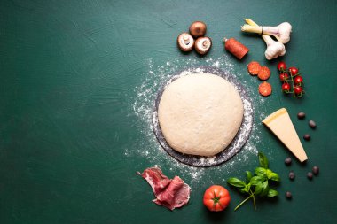 Pizza hamuru ve malzemelerle yeşil arka planda pizza hazırlıyorum. Pizza malzemelerinin ve hamurun üst görüntüsü. İtalyan pizzası tarifi yapıyorum..