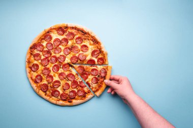 Bir kadının eli pepperoni pizzasından bir dilim alıyor. Bol etli nefis ev yapımı pizza. Dilimlenmiş pizza salamı, yukarıda.