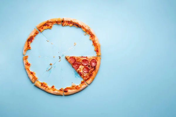 Pizza artıklarıyla ve pepperonili pizzanın son dilimiyle üst manzara. Pizzalı pepperoni dilimi mavi arka planda..